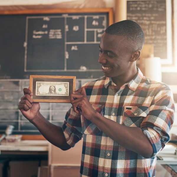 Man holding up $1 bill in frame and smiling.