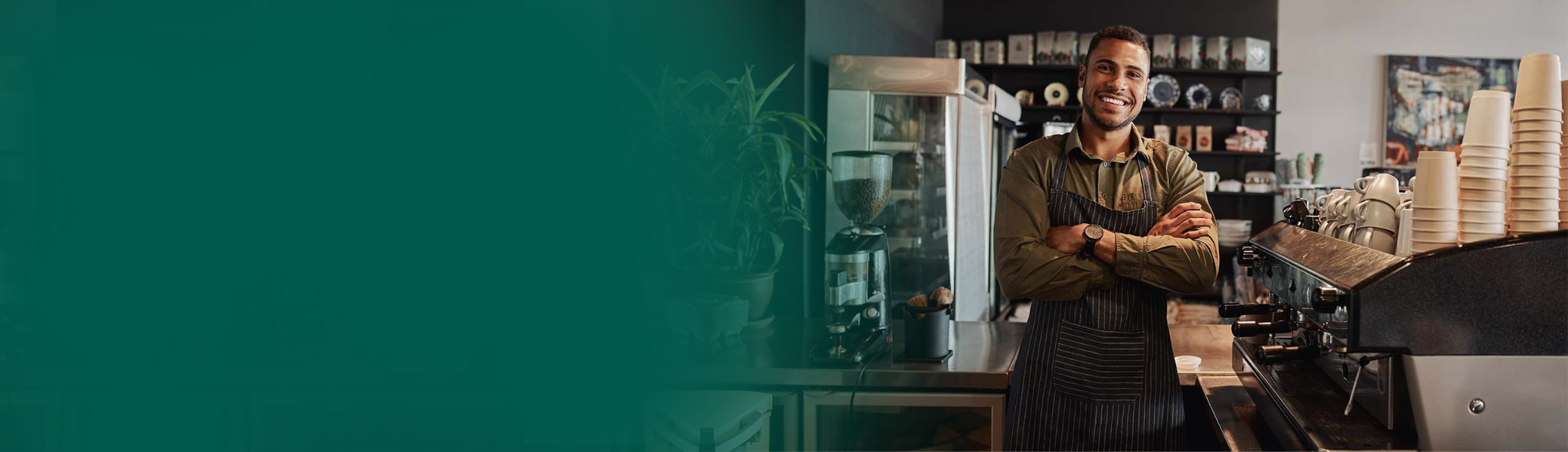 Coffee shop owner standing near his machines, arms crossed and smiling.