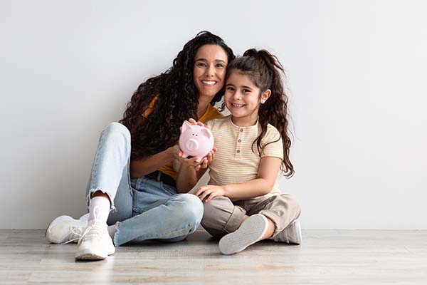 Mother and daughter sitting on the floor holding a piggy bank